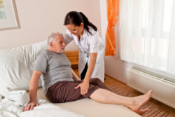 caregiver supporting an elderly man on bed